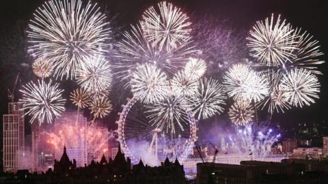 Fireworks skyline in london at new year - The London Eye is lit up surrounded by white explosions along the River Thames