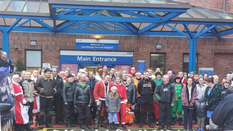 A group of motorcyclists, children and hospital staff stood in front of Scunthorpe General Hospital main entrance.