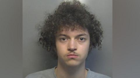 Kierson Murray mugshot wearing a grey t-shirt. He has brown eyes and very curly bushy hair. He  is starting at the camera.