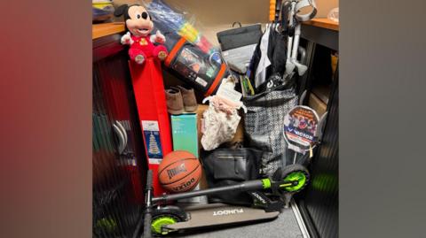 A number of items of lost property found on Tyne and Wear Metro trains. They include a folded scooter, a basketball, a tent and a windbreaker, both in packaging, a badminton racquet, a bag containing umbrellas and a crutch, plus a Mickey Mouse soft toy sitting on top of a Christmas Tree in a box.