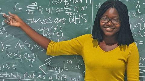 Angela Tabiri pointing at a blackboard with chalk calculations behind her