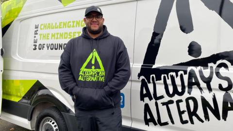 Anthony is stood in front of the mobile youth club, a purpose-built van. It's branded with Always An Alternative, and also reads "We're changing the mindset of young people."