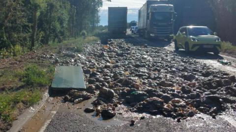 Food waste has been spilled across a single-carriageway road. Traffic is approaching on the right-hand side.