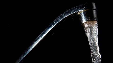 A silver mixer tap with water coming out, in front of a black background