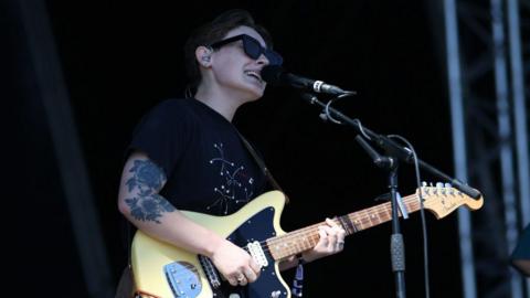 Bridie Monds-Watson of Soak performs during Day 1 of Victorious Festival at Southsea Common on August 26, 2022 in Portsmouth, England. She is wearing a black T-shirt and holding a guitar on stage singing into a microphone. 
