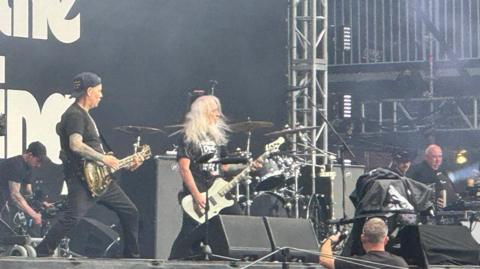 A rock band play on a stage holding guitars