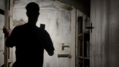 A silhouetted man standing in front of a bolted door 