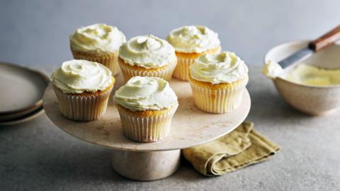 Size vanilla cupcakes with white frosting sit on a cake tray.