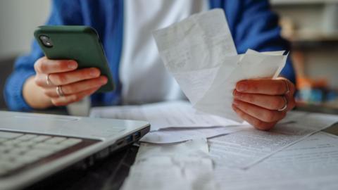 A stock image of someones hands holding receipts and a green phone.