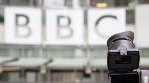 An image shows the BBC logo pictured on the entrance to BBC Broadcasting House in central London, with the top of a camera in the foreground, taken in March 2023