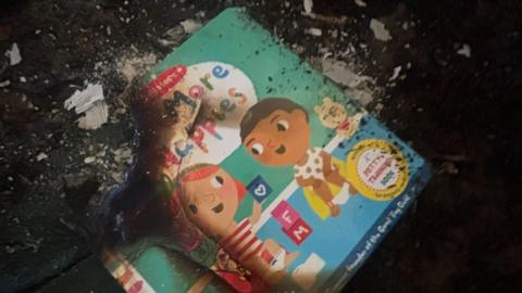 The remains of a children's book with two cartoon children on the front, which has been badly burned.
