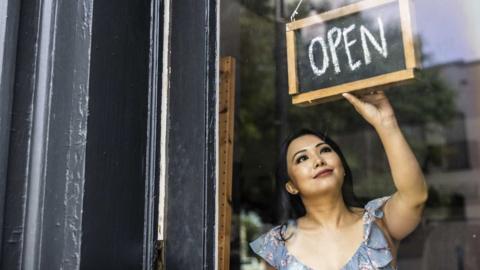 Female small business owner turning open sign in her shop