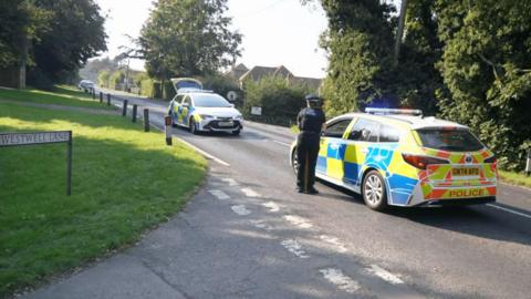 Two police cars are parked on a leafy, suburban road