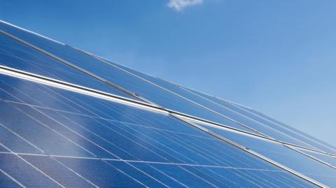 An aerial view of solar panels on the roof. The sky is blue and clear.