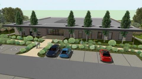 An artist design of what the facilities building would look like. A building span across the whole of the image and is made of grey bricks. There are six trees outside of the building and cars parked in a car park.