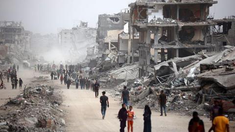 People walk down a street in Gaza City, rubble lines either side.