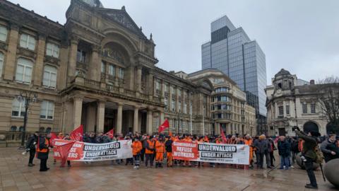 A large group of people standing outside Birmingham City Council, many of them wearing hi-vis clothing. People at the front are holding banners reading: "Birmingham refuse workers. Undervalued. Under attack."