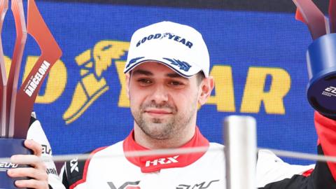 Ryan Cullen, wearing a Goodyear cap, pictured on a podium holding a trophy aloft