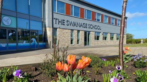 A building made out of brick and windows with orange and purple flowers int he brown flower bed at the front of the building.