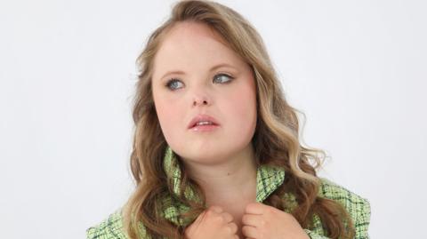 Beth Matthews is looking away from the camera and is holding the bottom of her green jacket's collars.