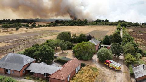 A drone view shows smoke rising in the distance as firefighters tackle a wildfire at Dunwich Heath