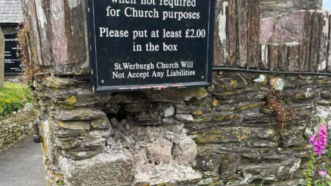 A stone wall with a hole and a sign above it.