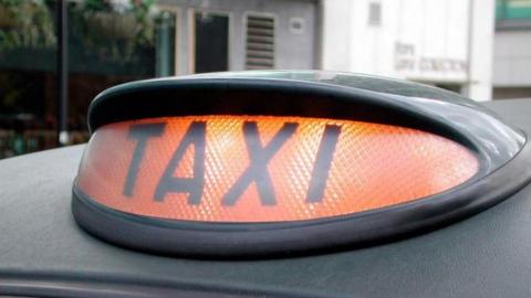 An orange light with black letters that reads taxi in a black casing