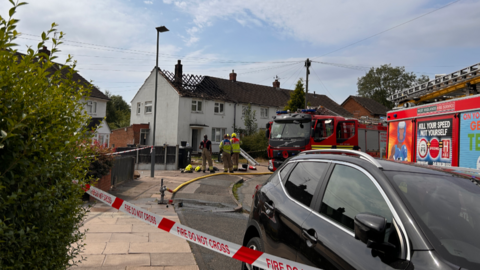 Firefighters outside an end terrace with burnt-out roof