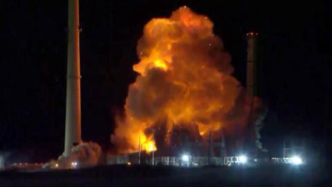 A huge fiery plume of smoke rises from a power plant at night. 