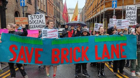 Campaigners march through Brick Lane carrying a large "Save Brick Lane" banner and placards opposing plans for data centres and calling for more homes.