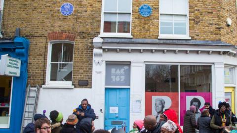 People gather as a blue plaque is unveiled for Darcus Howe at 167 Railton Road, Brixton