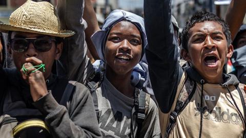 A close-up of three students chanting anti-government slogans.
