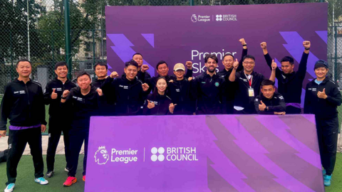 Jonathan Warburton in the centre, surrounded by Chinese grassroots coaches, standing next to large, purple Premier League advertising stands