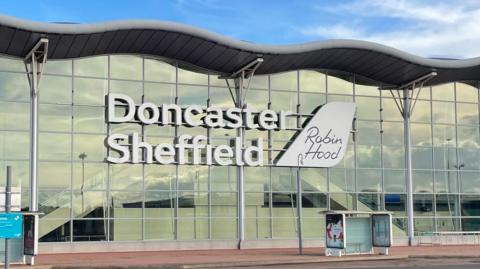 DSA terminal. A large glass fronted building with a wavy roof. With Doncaster Sheffield written in large white letters alongside a smaller sign saying Robin Hood