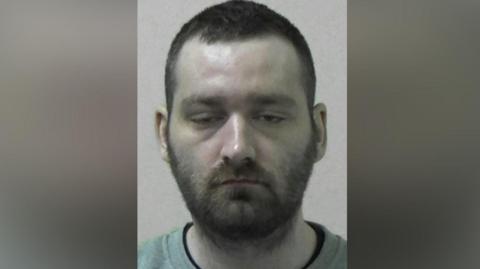 Mugshot of Jordan Reilly. He has his eyes half closed and has short dark hair and a beard.