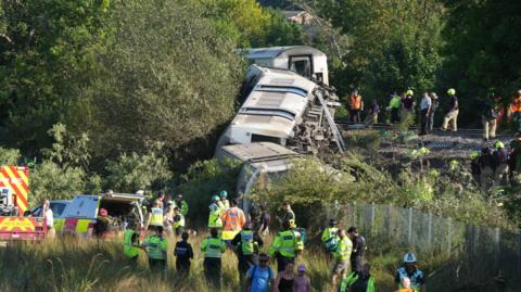 A group of people stood next to a derailed train.