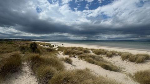 Patchy grey clouds above a beach with low sand dunes and grassy links 