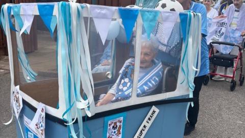 A woman with grey hair in a wheelchair with a homemade sky blue bus attached around the outside