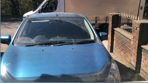 Dusty blue car parked on a driveway.