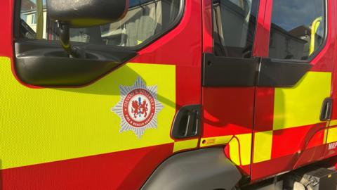 A red and yellow Devon and Somerset Fire and Rescue Service vehicle. The logo is on the side of the vehicle. 