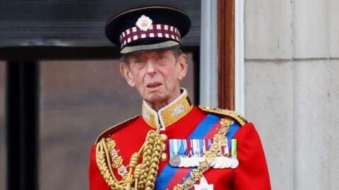 The Duke of Kent in a regal red royal uniform.