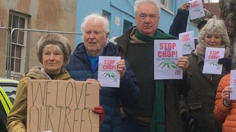 Campaigners gather on the pavement next to the three trees that are due to be felled