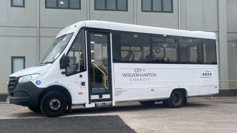 A white minibus parked infront of an office building. The minibus has a disabled badge on the front, with the writing city of Wolverhampton council on the side.
