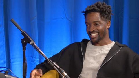 Guvna B sat at a podcasting studio and smiling