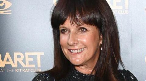 A woman with dark hair in a black sparkly dress poses in front of a backdrop for the Cabaret musical.