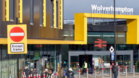 The view towards a yellow framed building, with the word Wolverhampton across the top. There are a number of people milling about outside