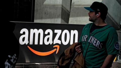A man wearing a green top walks past an Amazon sign on a street