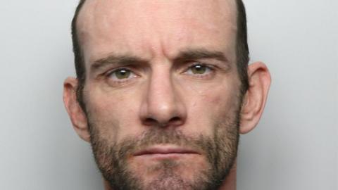 A police custody picture of a man with balding hair and a short beard.