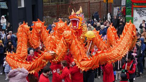 A long orange and golden dragon is paraded by performers in Liverpool, surrounded by spectators