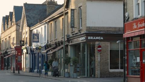 A view of Jericho's Walton Street businesses such as The Jericho Cafe and Branca restaurant. People can be seen walking in front, one man is pushing a pram.